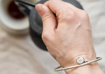 foto desde arriba donde se ve una mano de mujer sirviendose un cafe, en la mano lleva una pulsera de plata hecha a mano